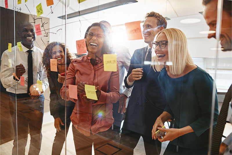 Group smiling while planning on a glass wall with post-it notes and marker