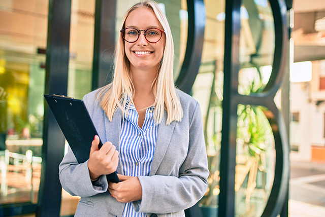 Professional blonde woman holding a clipboard and smiling at the camera